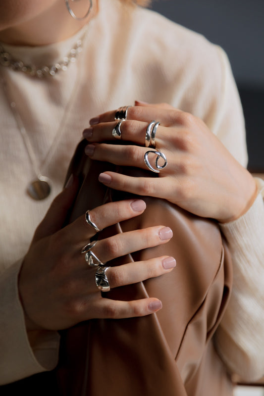 woman in white sweater and leather pants is sitting in a chair and has seven rings on her fingers