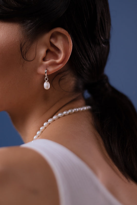 A brunette model in a white dress wore a pearl necklace and earrings and made a ponytail